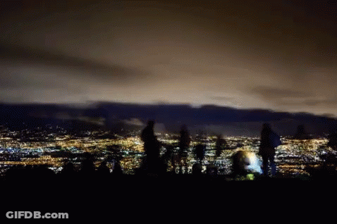 People Standing On Hill Over City At Night GIF
