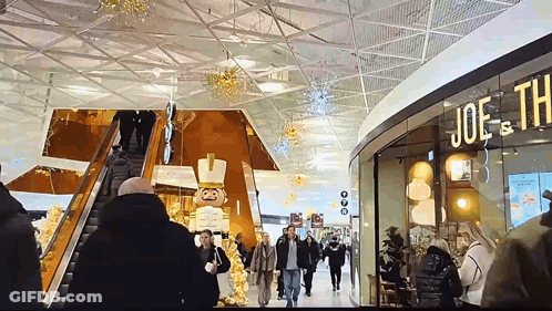 People Walking In A Shopping Mall With A Sign That Says Joe Th GIF