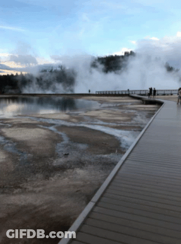 People Walking On A Boardwalk Overlooking A Body Of Water With Steam Coming Out Of It GIF