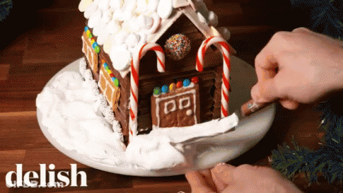 Person Decorating Gingerbread House With Candy Canes GIF