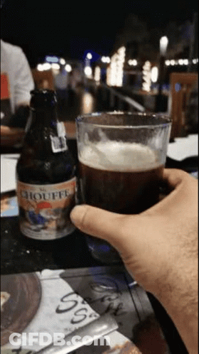 Person Holding Beer Beside Chouffe Bottle GIF