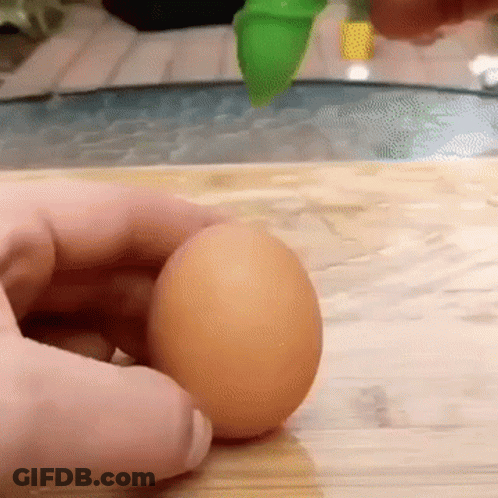 Person Holding Brown Egg On Wooden Cutting Board GIF