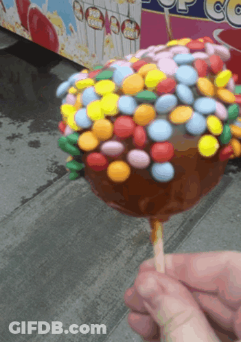 Person Holding Caramel Apple Covered In Colorful Candy GIF