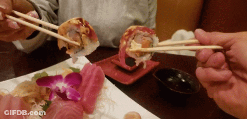 Person Holding Chopsticks Over Sushi GIF