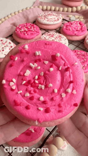 Person Holding Cookie With Pink Frosting And Sprinkles GIF