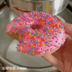 Person Holding Donut With Pink Frosting And Sprinkles GIF