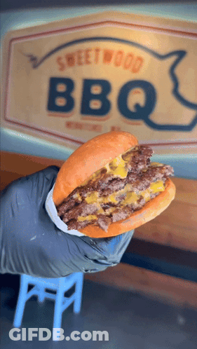 Person Holding Hamburger In Front Of BBQ Sign GIF