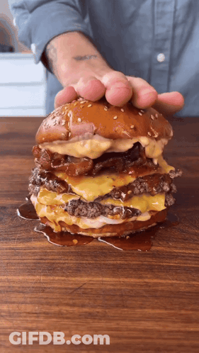 Person Holding Large Hamburger On Cutting Board GIF