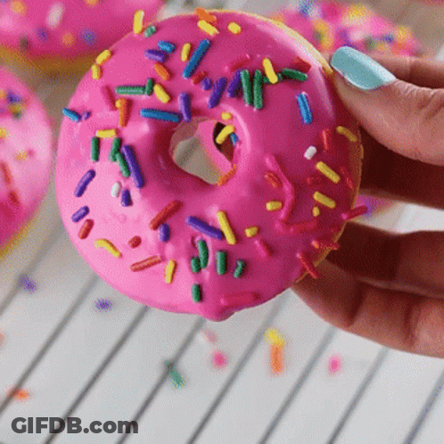 Person Holding Pink Frosted Donut With Sprinkles GIF