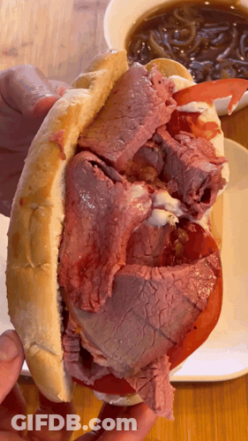 Person Holding Roast Beef Sandwich With Tomatoes And Onions GIF