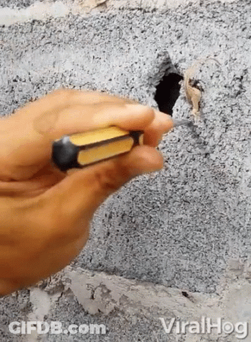 Person Holding Screwdriver At Hole In Concrete Wall GIF