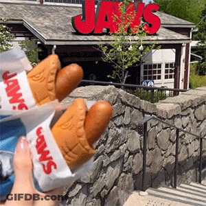 Person Holding Two Hot Dogs In Front Of Jaws Sign GIF