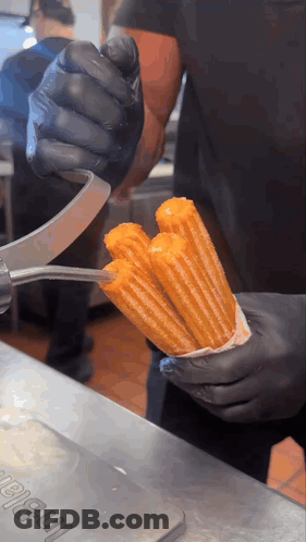Person In Black Gloves Holding Churro In Front Of I-Ball Sign GIF