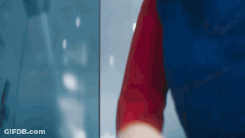 Person In Blue And Red Shirt Standing In Front Of Window GIF
