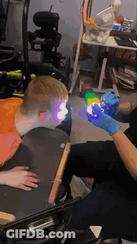 Person In Blue Gloves Holding Cube In Front Of Child In Wheelchair GIF