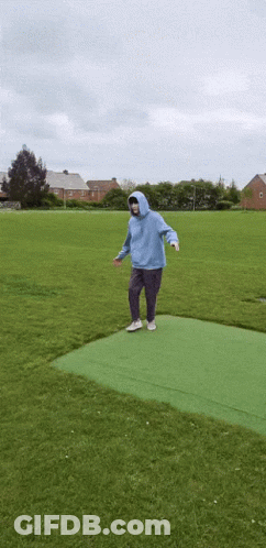 Person In Blue Hoodie Standing On Green Carpet In Field GIF