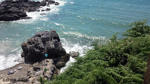 Person In Blue Shirt Standing On Rock Near Water GIF