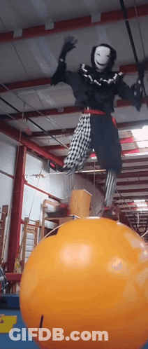 Person In Clown Costume Balancing On Orange Ball GIF