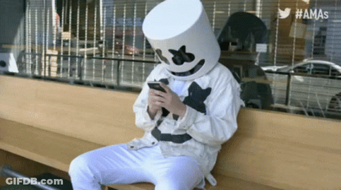 Person In Marshmallow Mask On Bench Looking At Phone GIF