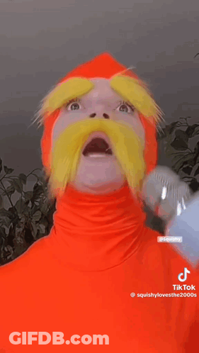 Person In Orange Costume With Yellow Mustache Holding Microphone GIF