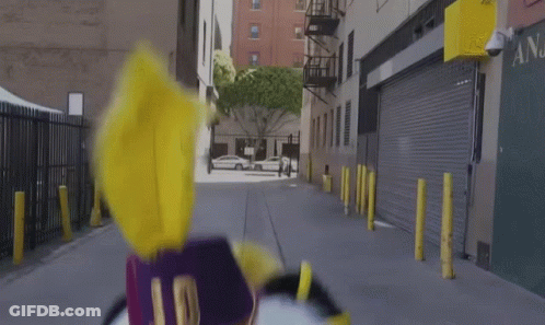 Person In Purple And Yellow Costume Walking Down Street GIF