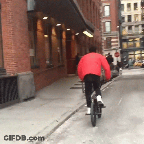 Person In Red Jacket Riding Bike Down Street GIF