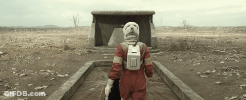 Person In Red Jumpsuit And White Helmet Walking Through Desert GIF
