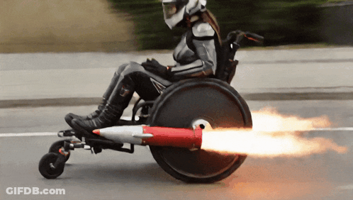 Person In Wheelchair With Rocket On Back Wheel GIF
