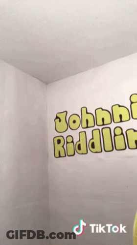 Person In Yellow Shirt In Front Of Johnny Riddler Wall GIF