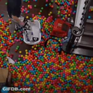 Person Laying In Pool Of Colorful Balls With Staircase GIF