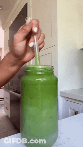 Person Pouring Green Liquid In Mason Jar With Straw GIF