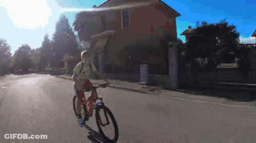 Person Riding Bike Down Street In Front Of Building GIF