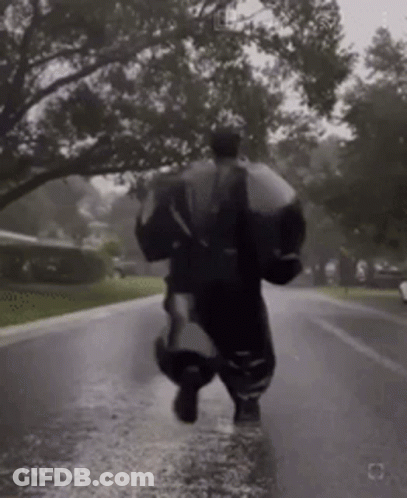 Person Running Down Wet Street With Umbrella In Rain GIF