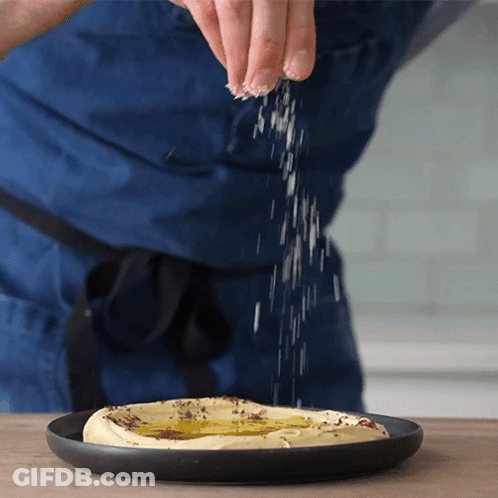 Person Sprinkling Salt On Hummus GIF