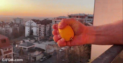 Person Squeezing Orange With City Pause (N) GIF
