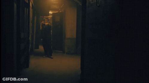 Person Standing In Dark Hallway With Light Behind GIF