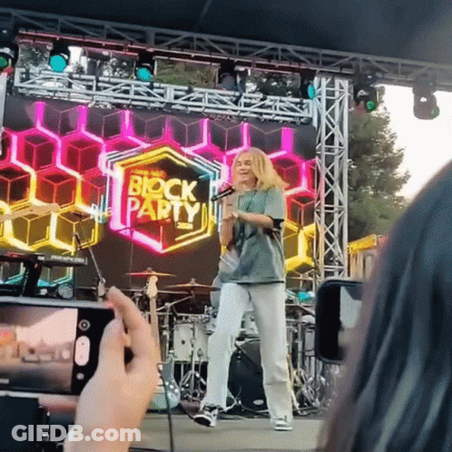 Person Taking Picture Of Girl On Stage With Block Party Sign GIF
