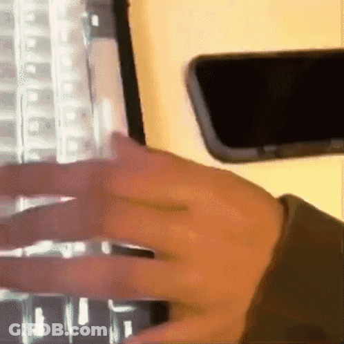 Person Typing On Keyboard Next To Phone GIF