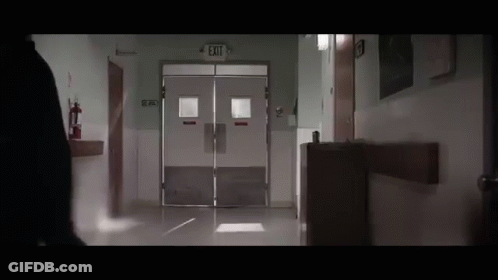 Person Walking Down Hospital Hallway With Exit Sign GIF