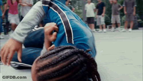 Person With Braids Lying On Ground As People Watch GIF