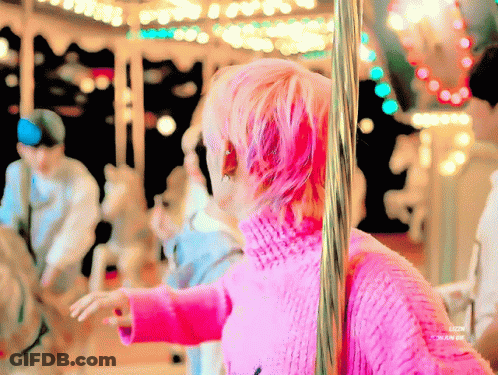 Person With Pink Hair In Front Of Merry Go Round GIF