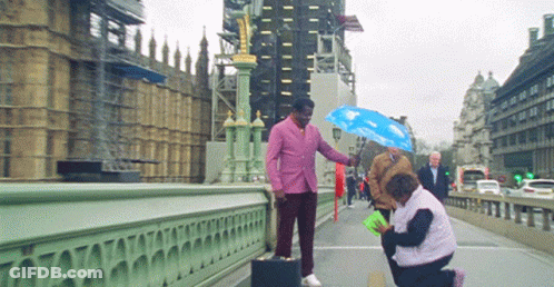 Pink-Suited Man Holds Blue Umbrella Over Woman Bridge GIF