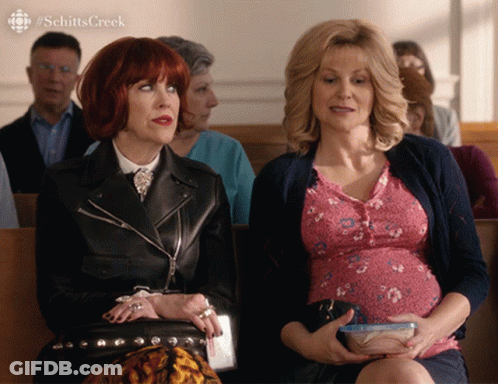 Pregnant Woman Beside Another In Church Schitt's Creek GIF