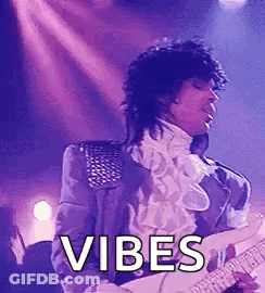 Prince Is Playing A Guitar On Stage While Wearing A Purple Jacket . GIF