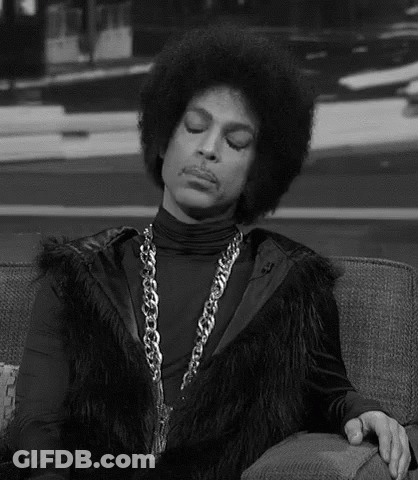 Prince Is Sitting On A Couch Wearing A Fur Vest And A Chain . GIF