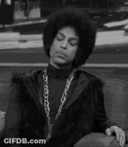Prince Is Sitting On A Couch With His Eyes Closed And Wearing A Fur Vest . GIF
