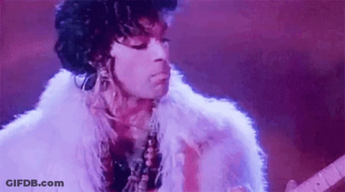 Prince Is Wearing A White Fur Coat And Playing A Guitar On Stage . GIF