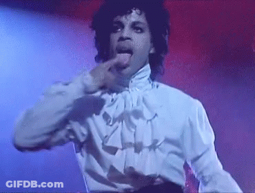 Prince Is Wearing A White Shirt And Ruffled Collar And Is Sticking His Tongue Out While Dancing On Stage . GIF