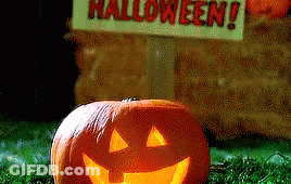 Pumpkin With Carved Face In Front Of Halloween Sign GIF