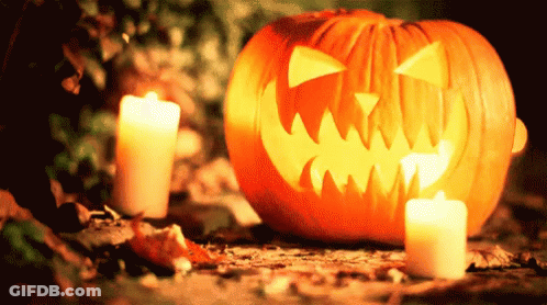 Pumpkin With Carved Face Next To Candles GIF